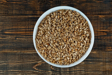 Sunflower seeds in a white bowl on an old shabby board. Nuts on a brown wooden table.