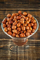 Hazelnuts in a transparent glass bowl on an old shabby board. Nuts on a brown wooden table.