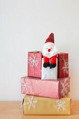Santa claus doll sitting on pile of presents which decorated with snowflakes on wooden floor and white background. Christmas and new year gift concept. Selective focus
