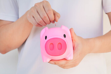 Closeup of hand putting coin into pink piggy bank Selective focus. Savings for education, travelling, retirement, tax,  hospitalization concept.