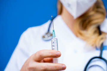 Nurse in front of a blue background holding a syringe and preparing the therapy to be injected to patients.