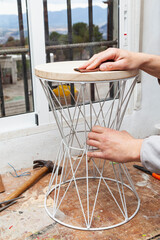 Fototapeta na wymiar The hands of a carpenter sanding a stool