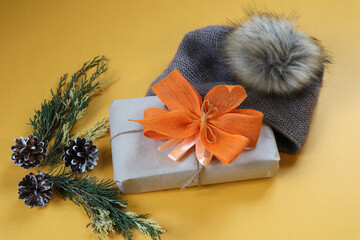 Fototapeta premium Christmas gift with yellow bows in winter gray hat on yellow background, top view, place for text
