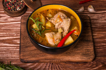 Deep plate with stewed potatoes and chicken meat on a wooden table