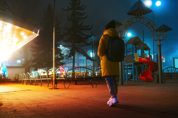 Back view. The girl is walking alone in the city at night. Fog, winter and night illumination. She...