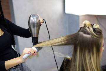 Professional woman hairdresser drying woman's hair styling using blow dryer at the hairdressing...