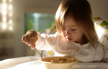 Two years old eats porridge by herself with a spoon. Child development concept
