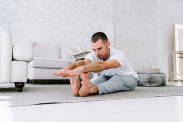 Young caucasian male in casual wear bending stretching neck muscles during morning workout,...