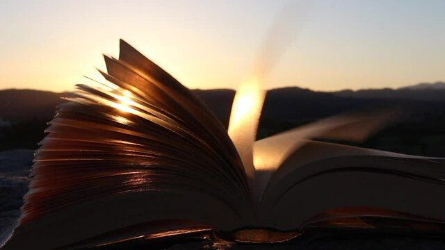 Inspiration and wisdom concept. Open book with pages moving in the wind at sunset or sunrise sunlight, warm light.