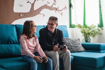 Obraz premium Grandfather plays video games with his granddaughter in the living room.