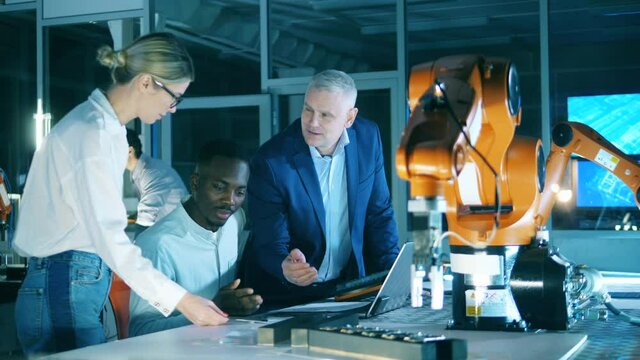 Two engineers explaining the third one industrial robot functions and add ons. Innovation, modern technology, futuristic laboratory concept.