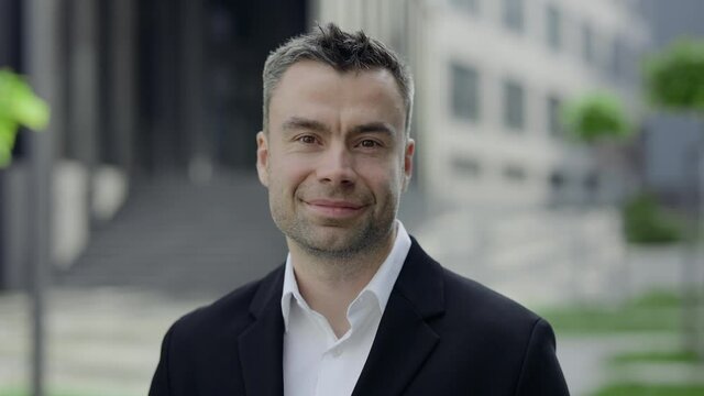 Portrait of cheerful mature businessman turning head and looking to camera. Crop view of happy male person wearing formal outfit posing outdoors. Concept of business.