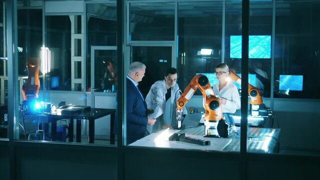 Three engineers discussing industrial robot capabilities at laboratory. Team of industrial robotics engineers working with robot arm.
