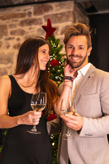 Romantic New Years dinner for a young Caucasian couple. Toasting with the winged champagne glasses of the Christmas tree