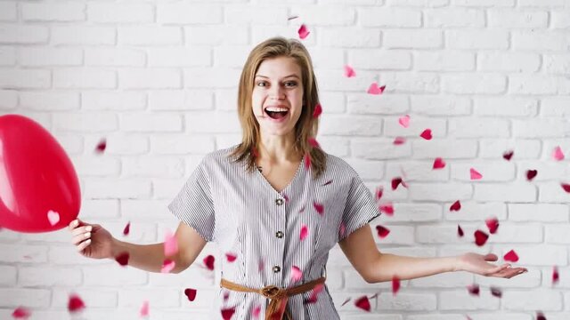 Valentine's Day. Young woman blowing red heart shaped confetti