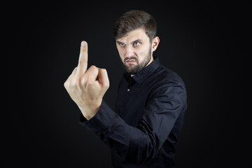 a man in a black shirt and on a black background shows his middle fingers makes obscene gestures