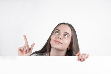 Fototapeta premium Teenage girl shows thumb up and smiles while holding white blank paper.