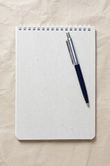  Gray notepad with white coiled spring and pen on a background of beige crumpled craft paper