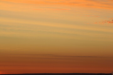 Sun below the horizon and clouds in the fiery dramatic orange sky at sunset or dawn backlit by the...