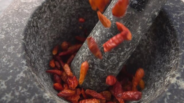 Super close-up of red cayenne pepper pods falling into the stone mortar in slow motion