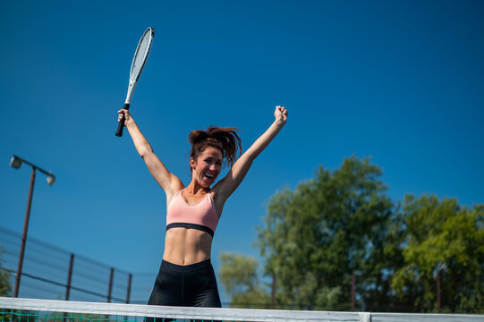 The female winner celebrates her tennis success. The happy girl is jumping on outdoors tennis court.