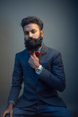 Portrait of young man posing with beard in suit on gray background.