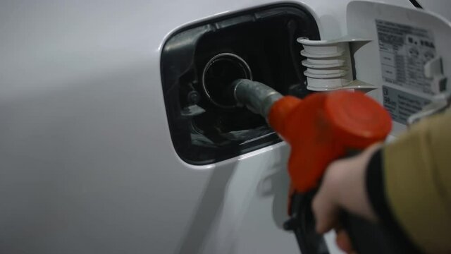 The guy finishes refueling his car by shaking off and pulling out the refueling gun. Close-up