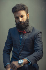 Portrait of young man posing with beard in suit on gray background.