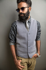 Bearded young businessman posing with sunglasses on gray.