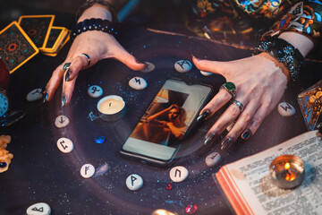 The fortune teller casts a spell on a smartphone with photo. Hands and device close-up. The view...