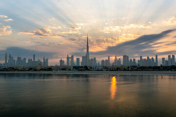 Sunrise in Dubai with cloudy sky view from boat or sea. The Sun rises over UAE skyscrapers at morning. Dubai beach, coast, shore