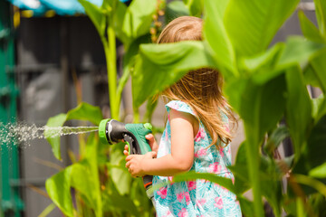 2-3 year old girl with garden hose water the plants plants. Activity for chirldren at summer concept.