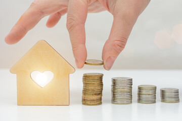 on a light background stacks of coins and a house. Hand adding a coin. The concept is the...