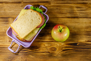 Lunch box with sandwiches and apple on a wooden table. Top view