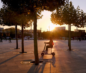 Young man riding a scooter in the light of the sunset on the street And young people ride on an...