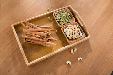 wooden tray of cardamom, cinnamon and cashew on wooden table.