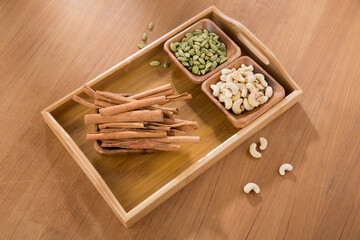 wooden tray of cardamom, cinnamon and cashew on wooden table.