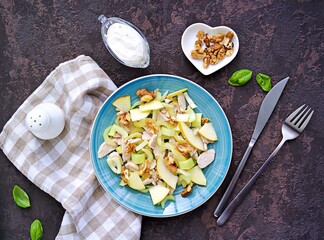 A healthy salad of stem celery, apples, boiled turkey or chicken and walnuts on a blue plate on a dark concrete background. Recipes of vegetable salads. Diet, detox. Top view.