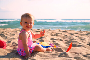 Happy baby in the sand plays. Cheerful little kid playing on the beach on a sunny day. High quality photo