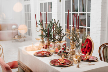 Festive table setting for Christmas. Red and gold shades. Blurred background.Stylish table setting with burning candles and Christmas decorations.