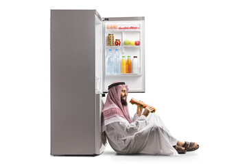 Happy saudi arab man eating a sandwich and leaning on a fridge