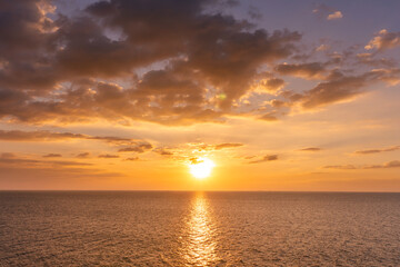 Fototapeta premium Sunset reflection ocean. beautiful sunset behind the clouds and blue sky above the over ocean landscape background
