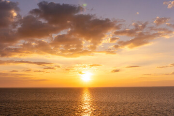 Fototapeta premium Sunset reflection ocean. beautiful sunset behind the clouds and blue sky above the over ocean landscape background