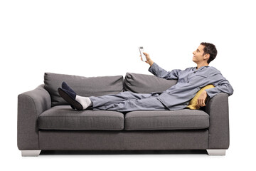 Man in pajamas laying on a sofa and holding a remote control