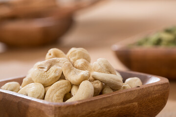 wooden bowl of cardamom, cinnamon and cashew on wooden table.