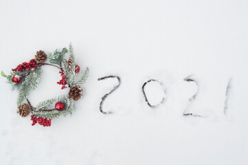 Beautiful New Year card with the numbers 2021 inscription, red balls and a snow-covered fir wreath on the snow