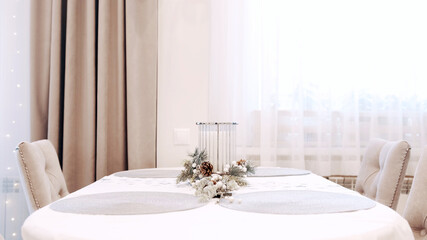 Brunette girl in white dress puts a beautiful Christmas candle on the dining table