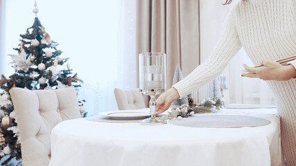 A girl in a white dress serves plates at the Christmas table. Festive table setting