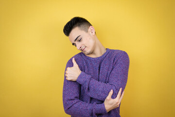 Young caucasian man over isolated yellow background hugging oneself happy and positive, smiling confident