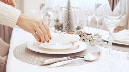 The girl with red nails put the festive napkin on the plates. Christmas table setting